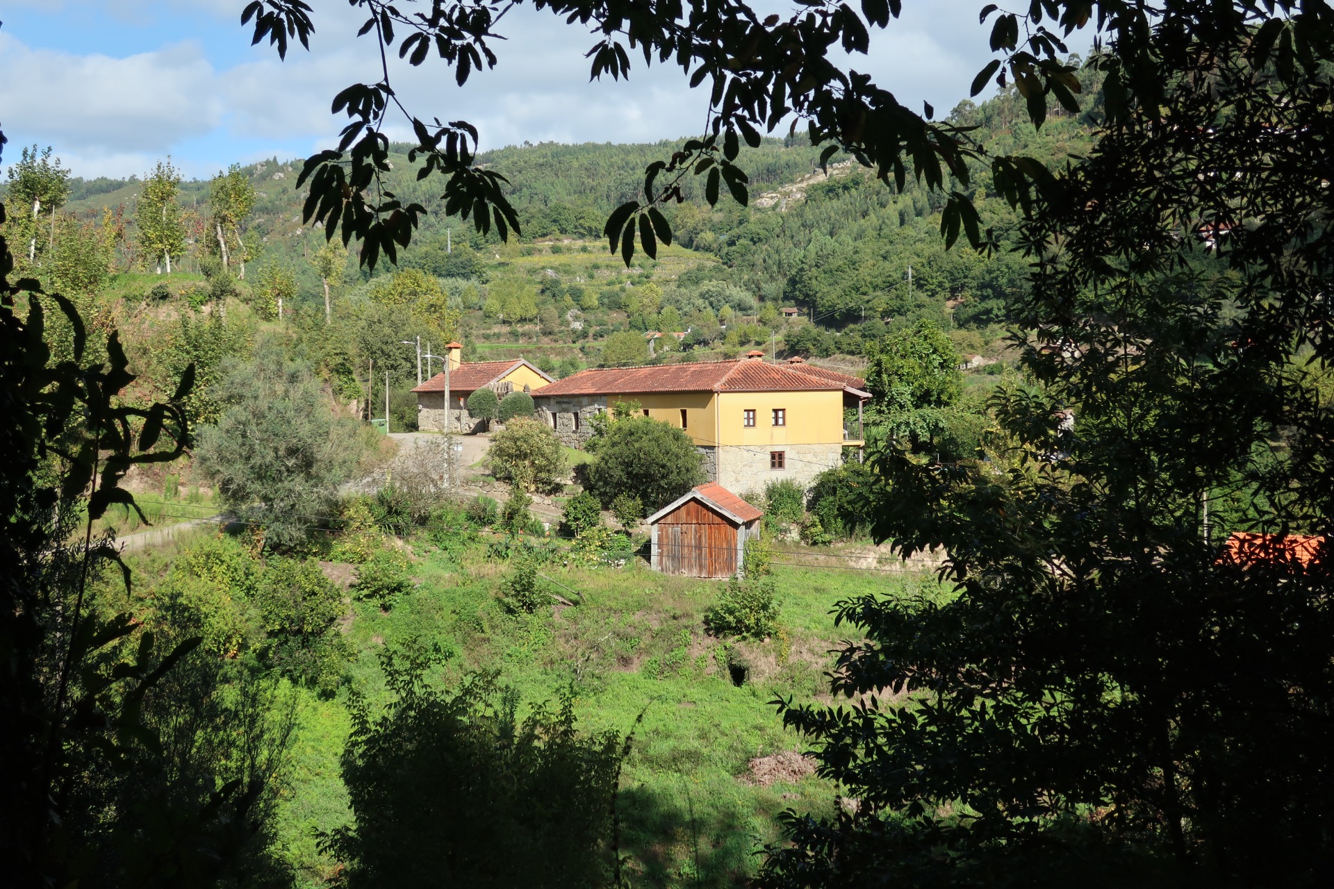 A casa vista ao longe, entre árvores e montes